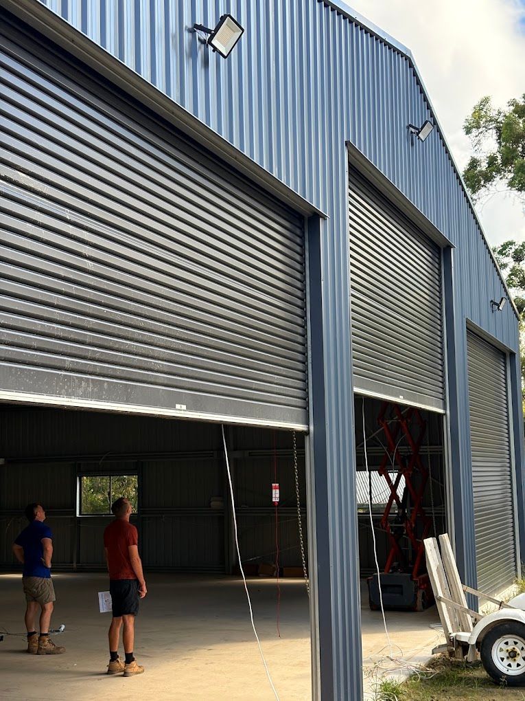 Floodlights mounted high on a large steel shed with its roller doors open